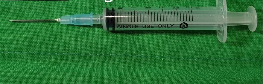 A 23 gauge needle on a 3 mL syringe, photographed on a green drape